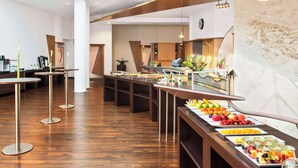 A modern hotel lobby with a buffet area featuring a variety of fruits and a marble wall. - NH Mannheim-Viernheim (Viernheim)