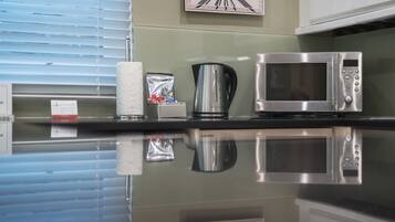 Una cocina con un microondas de acero inoxidable, una tetera y un reloj en la pared.