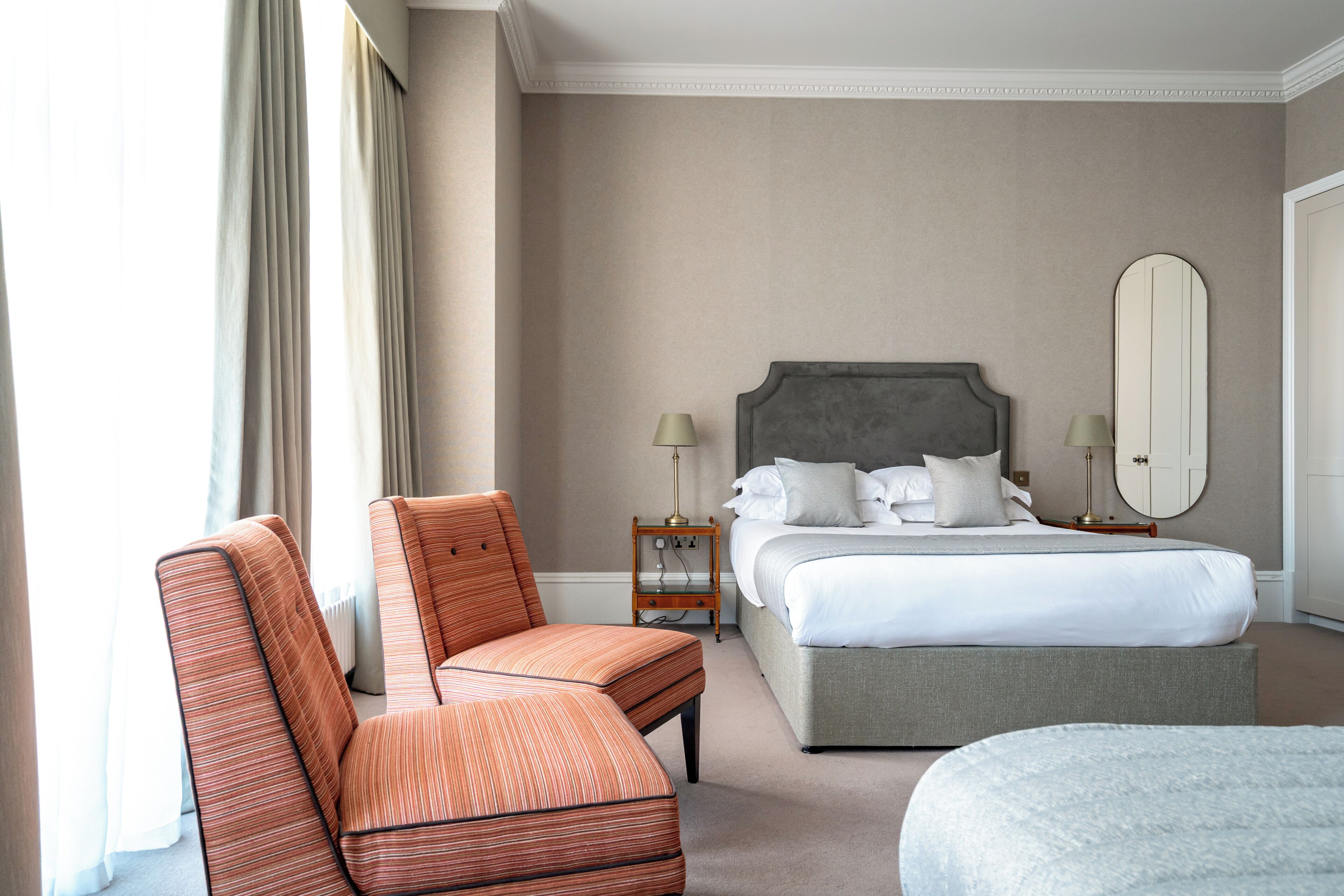 Una habitación de hotel con cama, una silla, una mesita de noche con lámparas y un espejo grande.