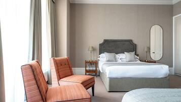 Una habitación de hotel con cama, una silla, una mesita de noche con lámparas y un espejo grande.
