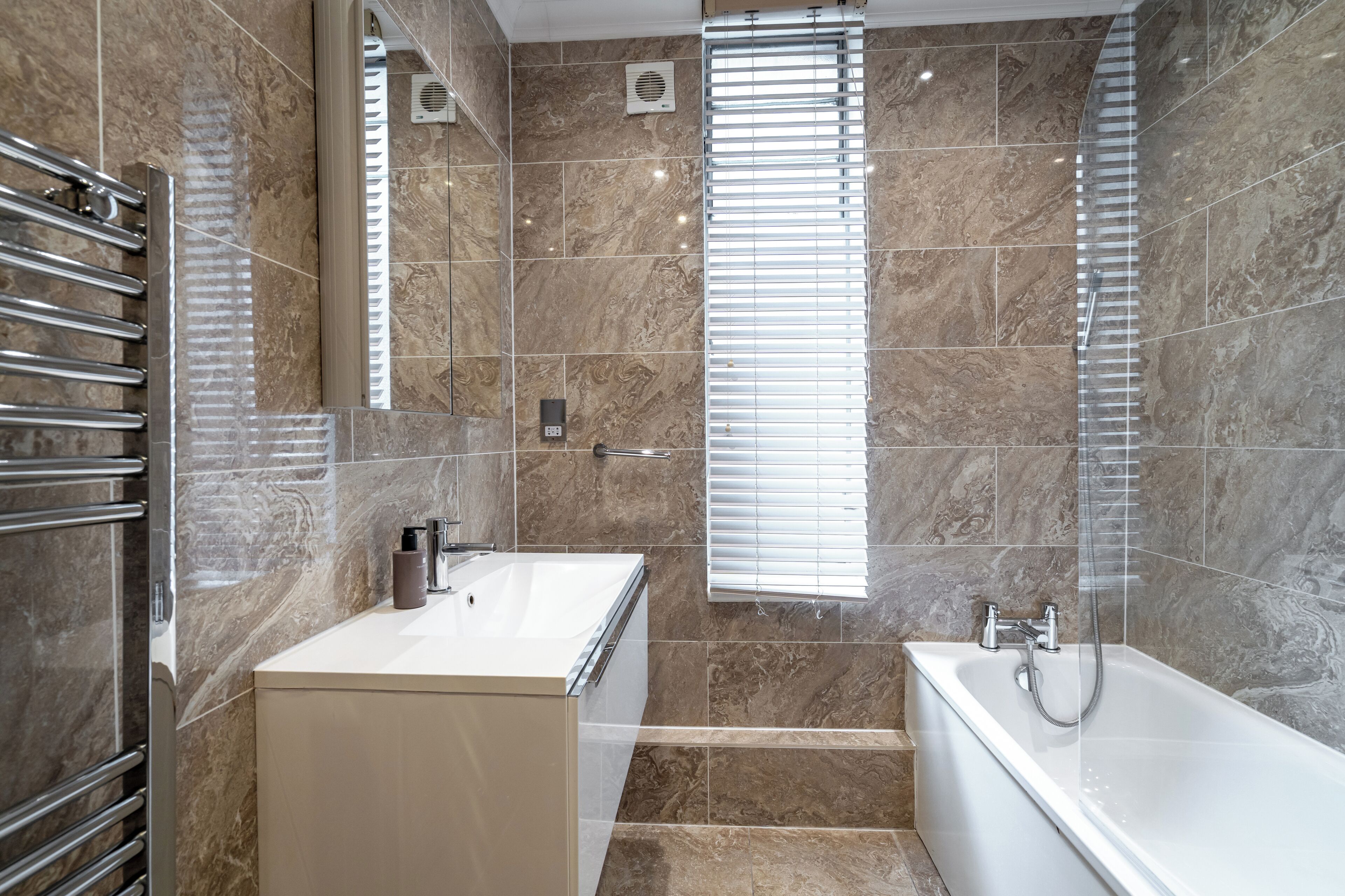 A modern bathroom with a marble-tiled wall, a white sink, a bathtub, and a shower with a glass door.
