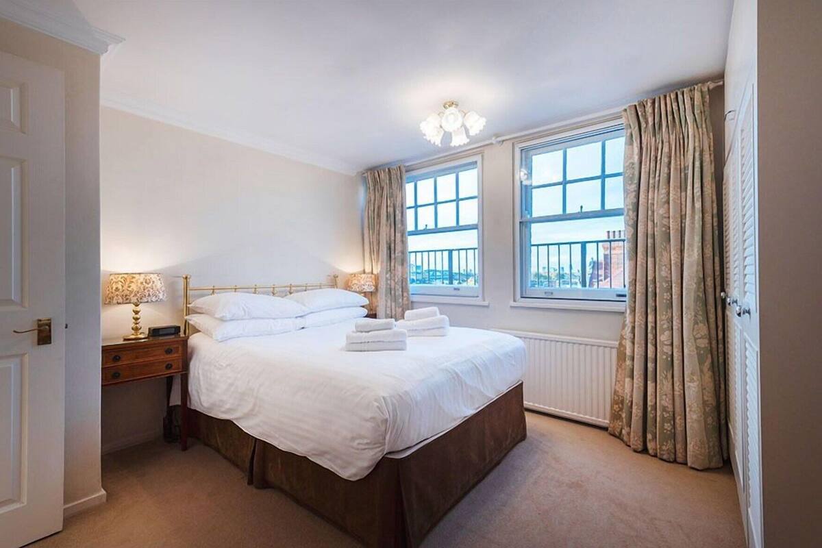 Une chambre à coucher avec un lit, des tables de chevet, une fenêtre avec des rideaux et un radiateur.