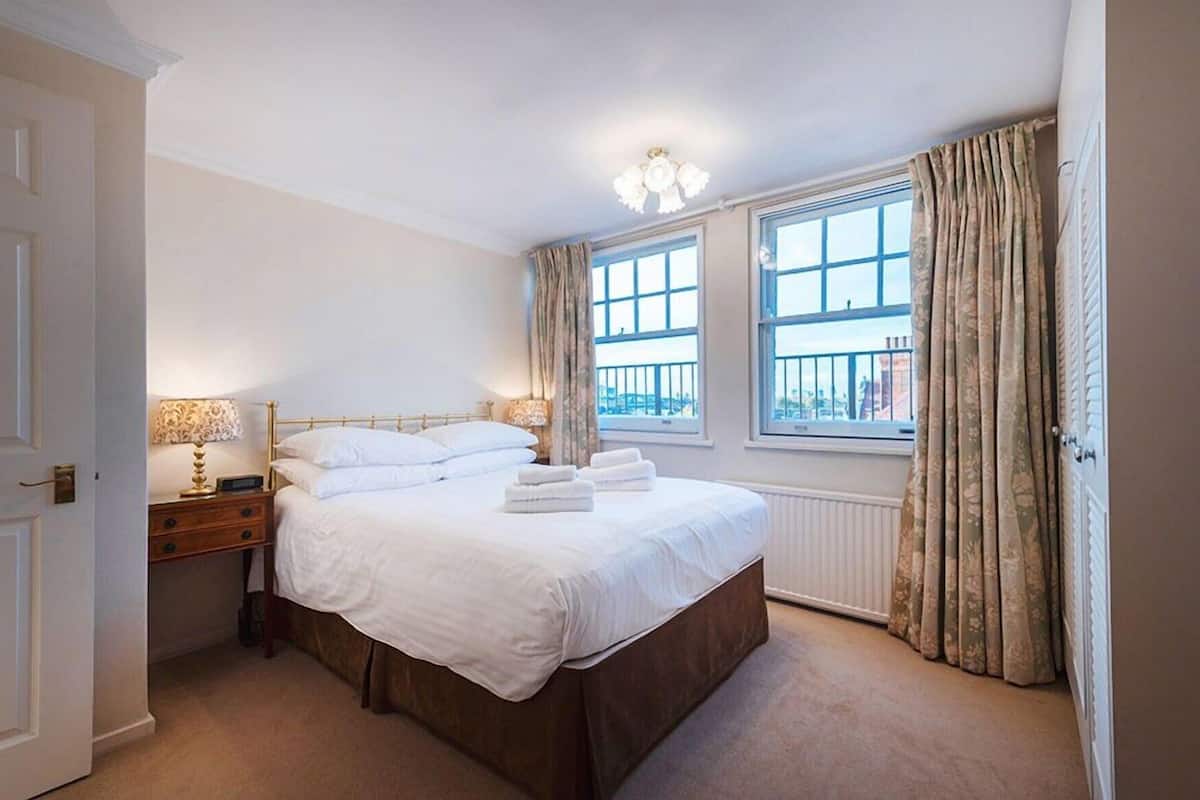 A bedroom with a bed, bedside tables, a window with curtains, and a radiator.