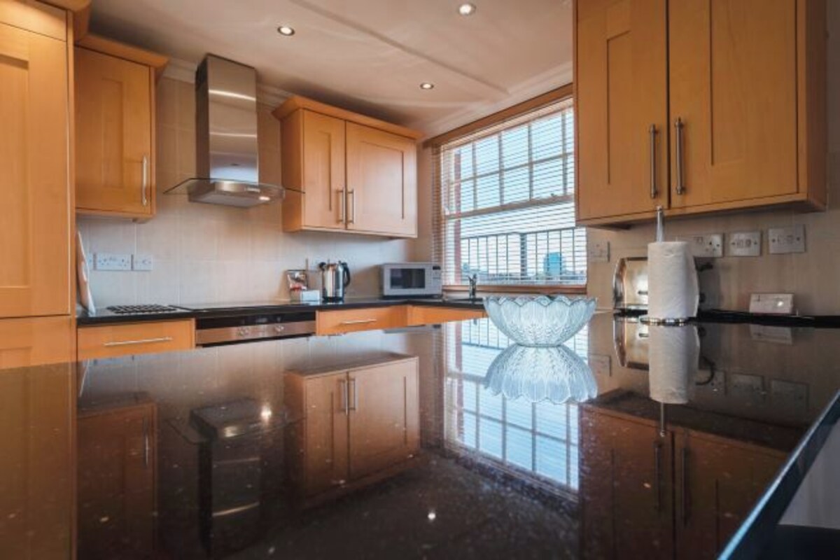Een moderne keuken met houten kastjes, een roestvrijstalen afzuigkap, een magnetron en een groot raam dat voor natuurlijk licht zorgt.
