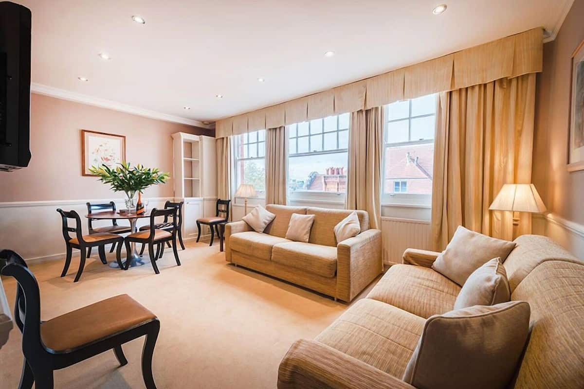 Un salon comprenant un canapé, des fauteuils, une table à manger avec des chaises et un téléviseur fixé au mur.
