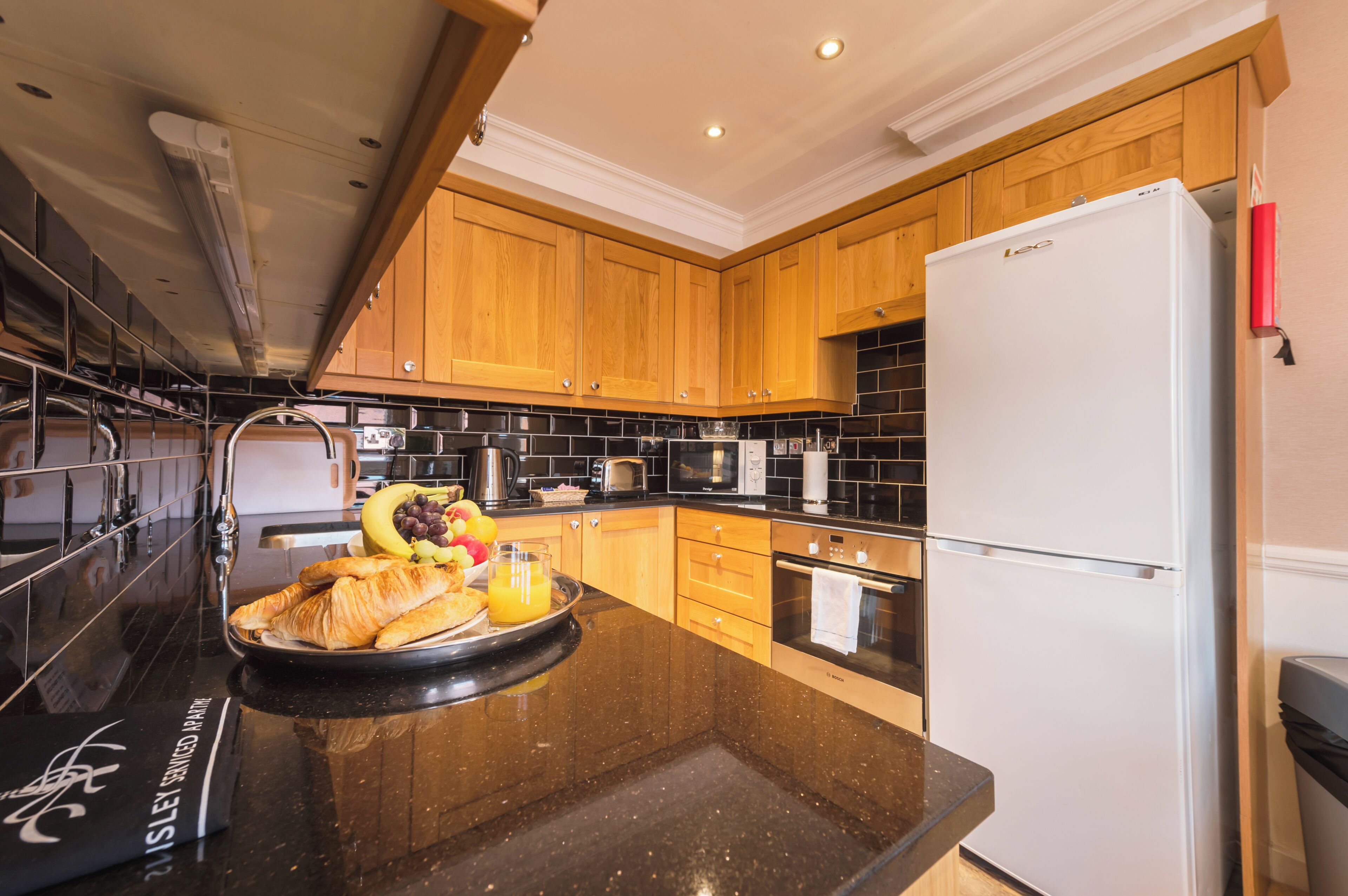 Una cocina moderna con armarios de madera, encimera negra y refrigerador blanco.