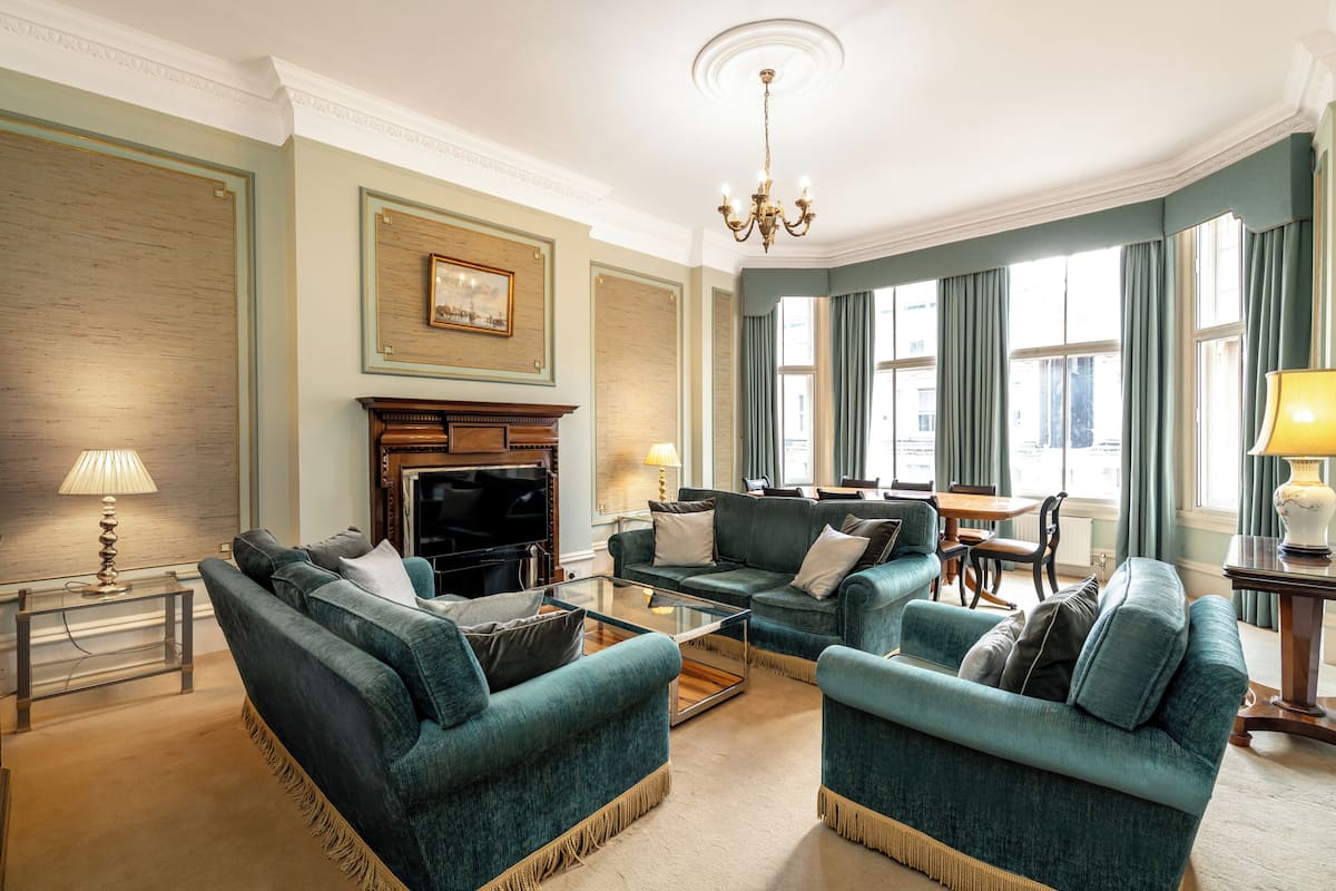 Un salon spacieux avec des canapés de couleur turquoise, une cheminée et de grandes fenêtres ornées de rideaux.