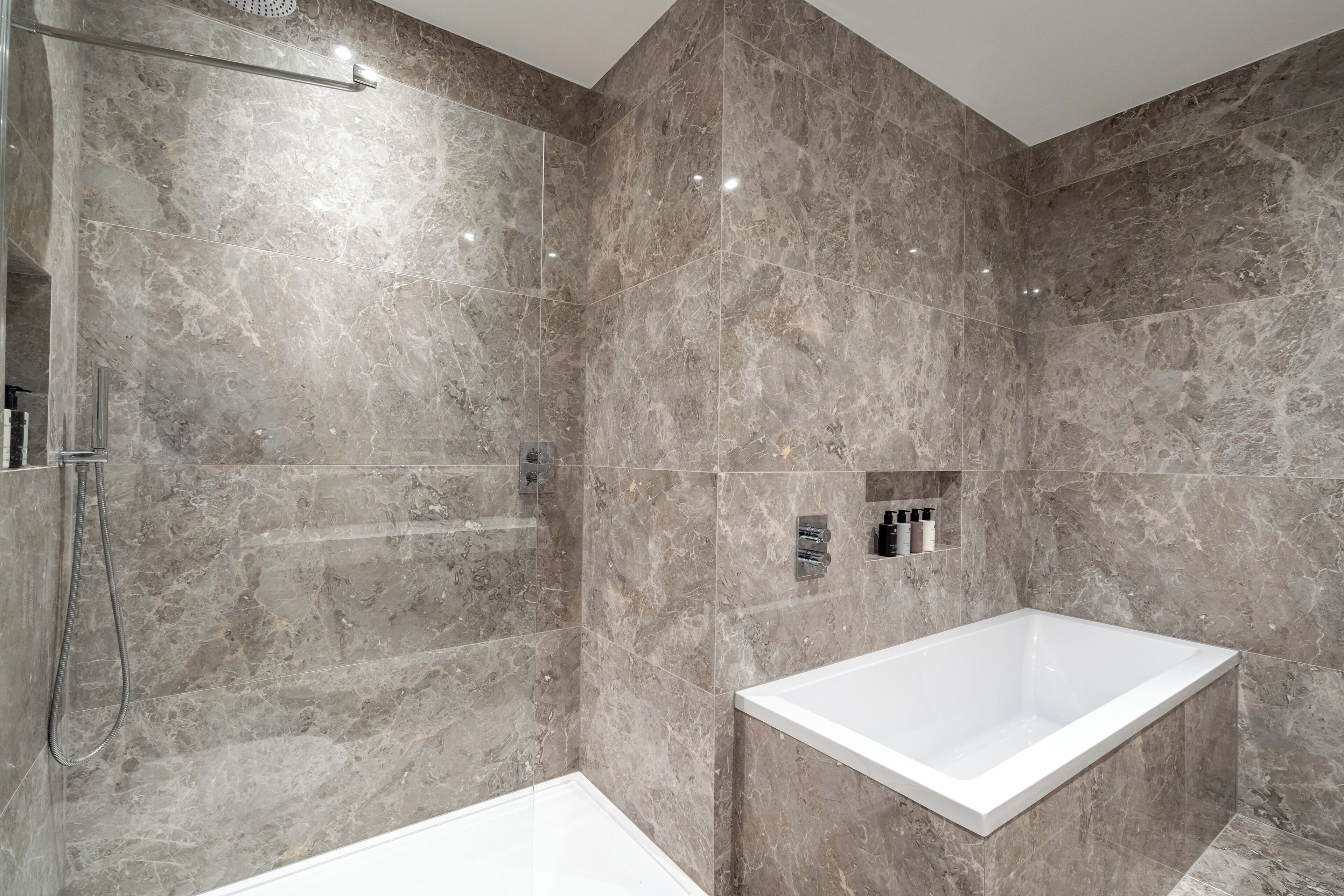 A modern bathroom with a walk-in shower, a standalone bathtub, and marble walls.