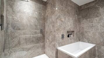 A modern bathroom with a walk-in shower, a standalone bathtub, and marble walls.
