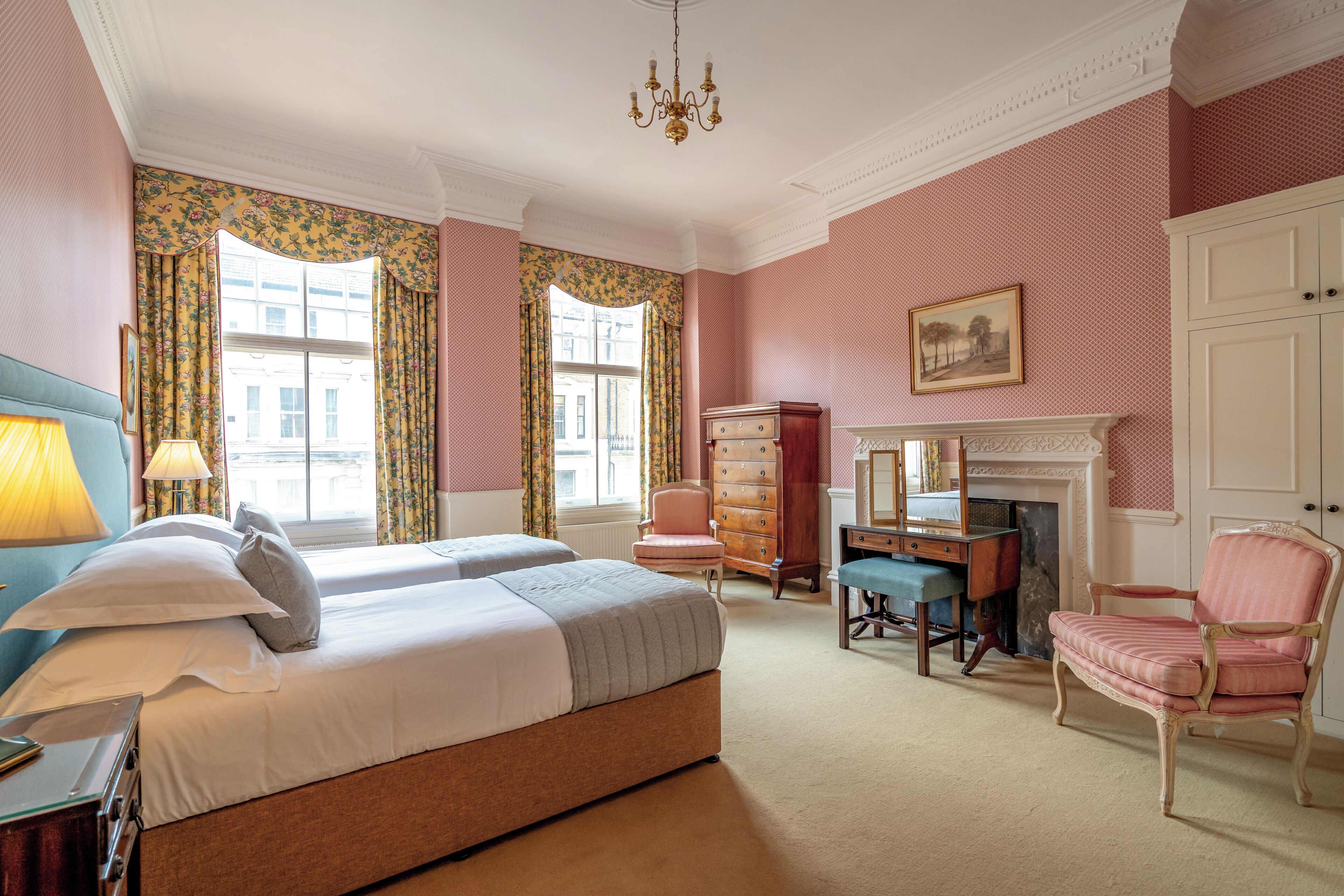 A bedroom with two beds, a dresser, a chair, a desk, and a fireplace.