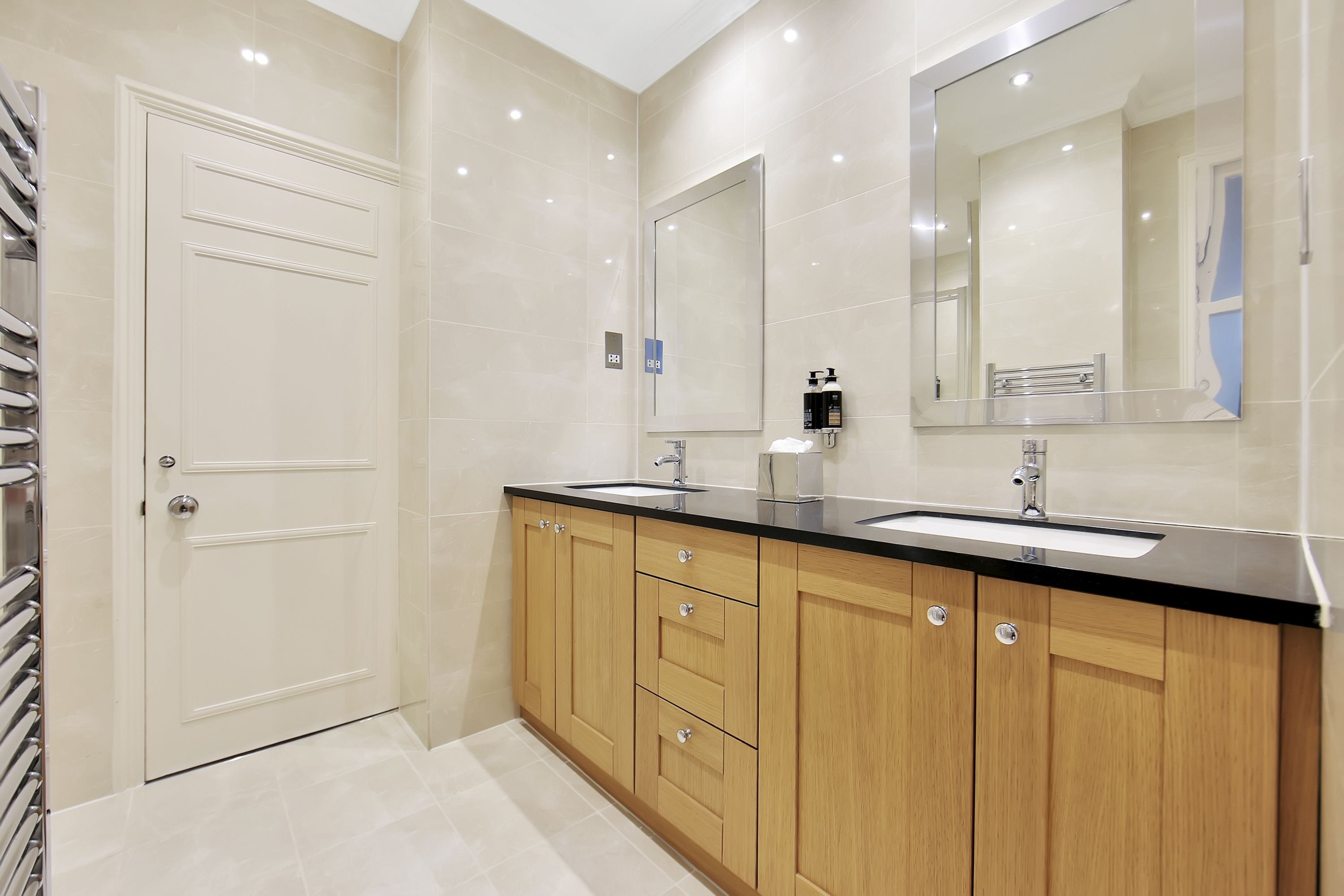 A modern bathroom with two sinks, wooden cabinets, and a large mirror.