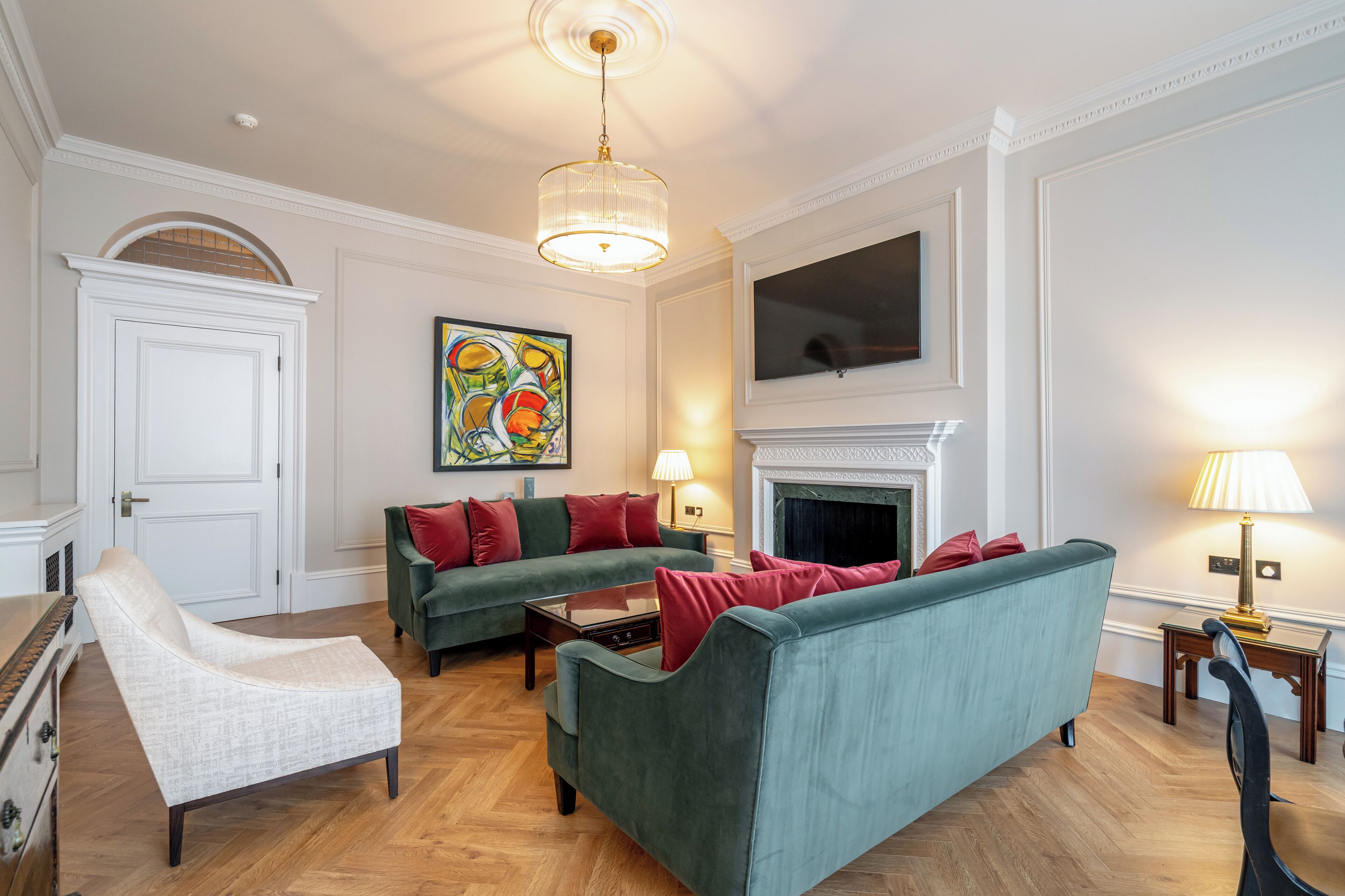 A living room with a green sofa, a white armchair, a fireplace, and a painting on the wall.
