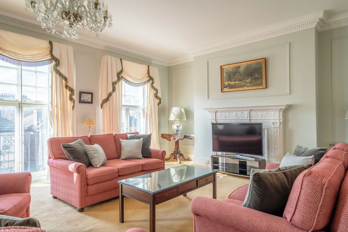 Un salon avec un canapé rose, une table basse en verre, une cheminée et un téléviseur.