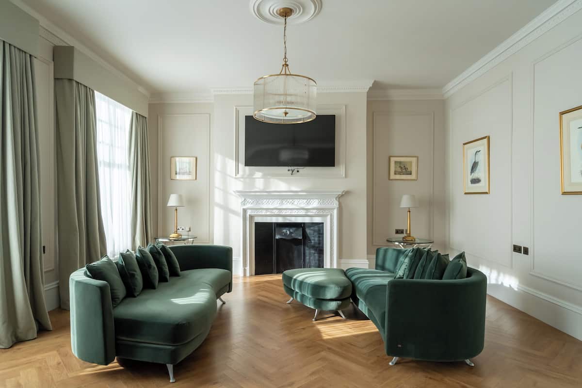 Un salon spacieux avec une cheminée, deux canapés verts et un grand téléviseur fixé au mur, juste au-dessus de la cheminée.