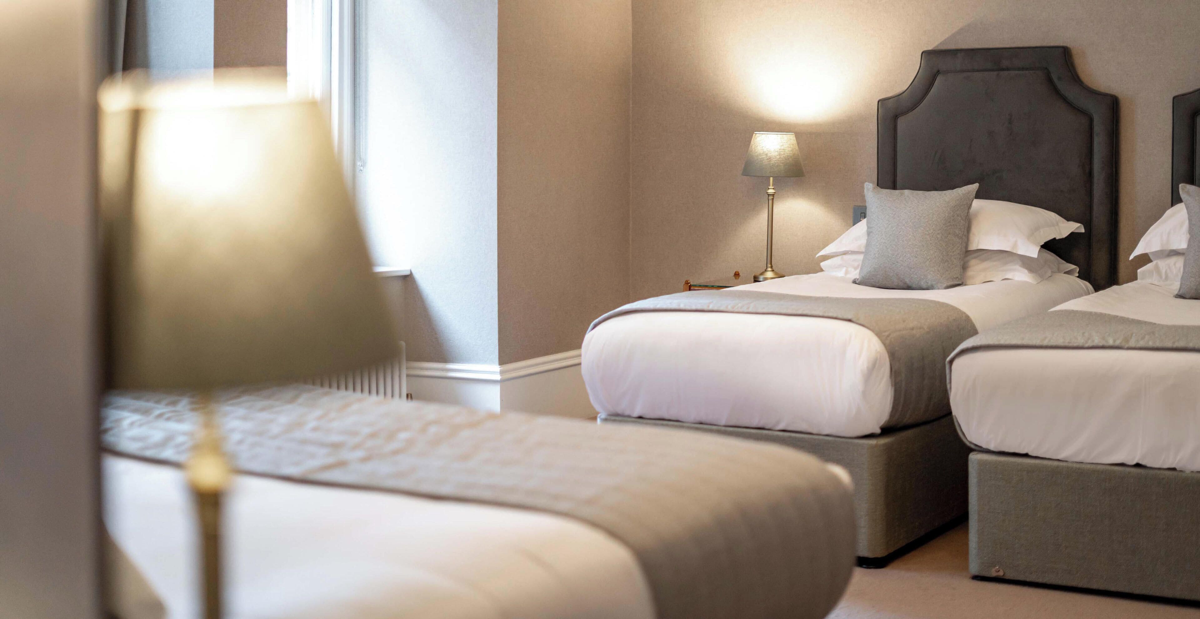 Une chambre d’hôtel avec deux lits, une table de chevet avec une lampe et une fenêtre.