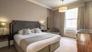 Une chambre d’hôtel avec un grand lit, deux lampes de chevet, une table de chevet, une commode, une fenêtre avec des rideaux et un radiateur.
