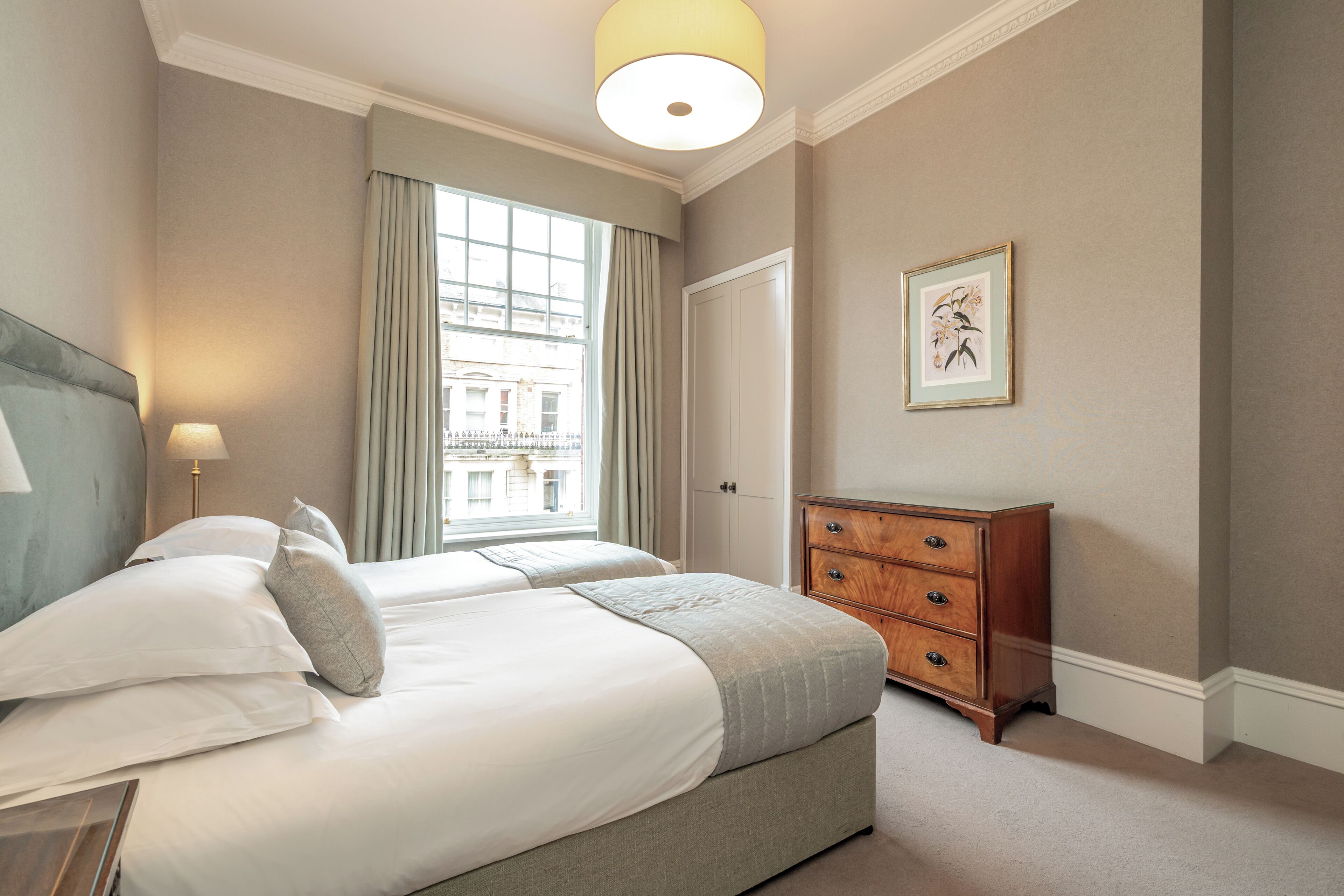 Hotellihuone, jossa on suuri sänky, puinen lipasto, seinällä oleva taulu ja ikkuna, jossa on verhot.