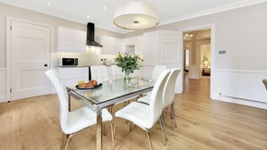 Une cuisine moderne avec des meubles blancs, une table à manger en verre et un luminaire suspendu.