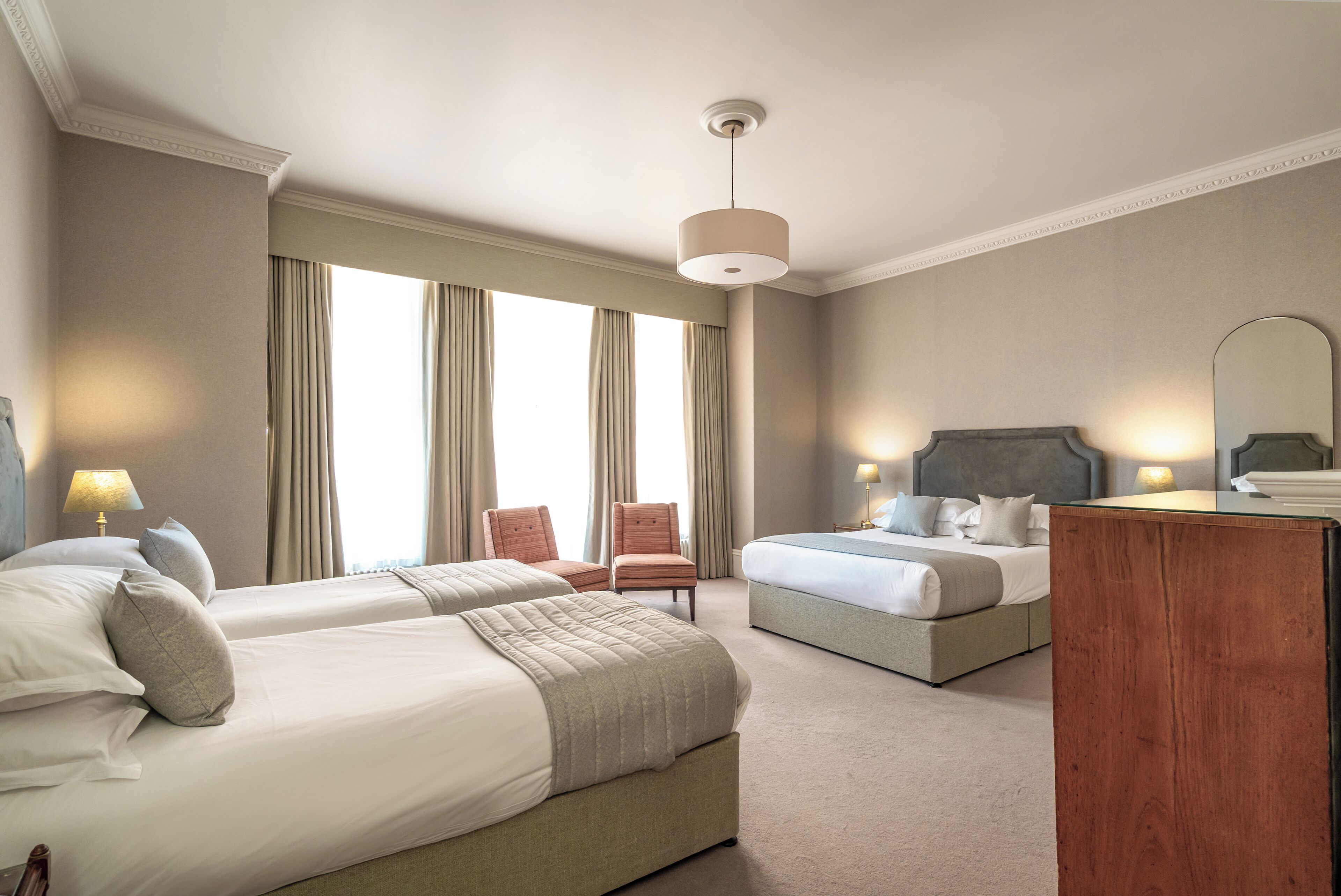Une chambre d’hôtel avec deux lits, un coin salon et une grande fenêtre avec des rideaux.
