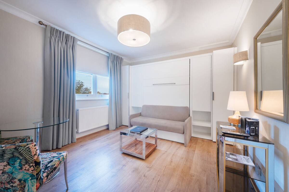 Un salon moderne avec un canapé, une table basse en verre, une table d’appoint avec une lampe et un grand miroir.