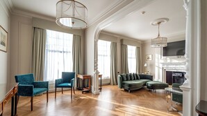 Un salon spacieux doté d’un parquet en bois, d’un canapé vert, de fauteuils turquoise et d’une cheminée.