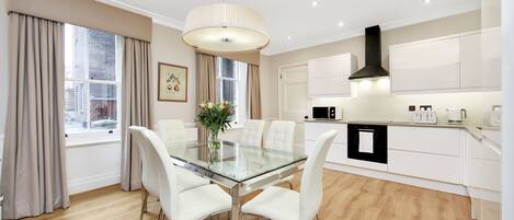 A modern kitchen with white cabinetry, a black range hood, and a glass dining table with white chairs.