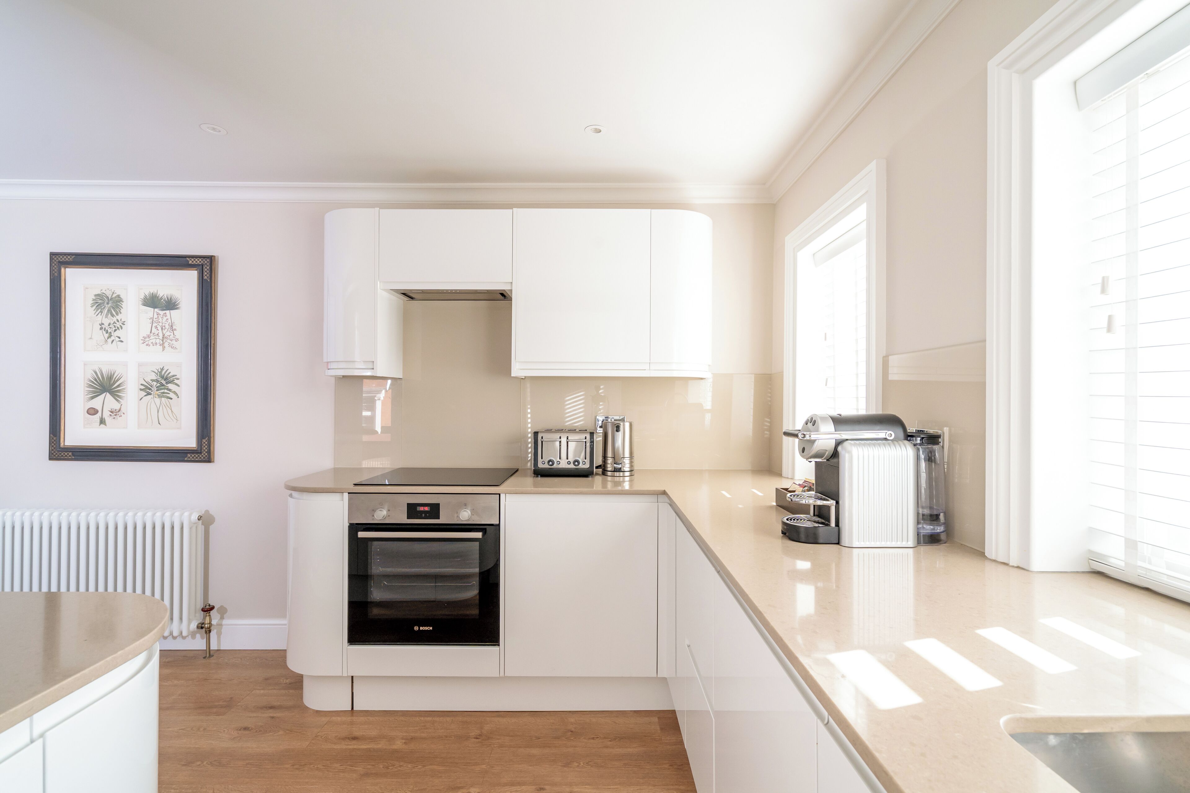 A modern kitchen with white cabinets, a Bosch oven, a toaster, and a coffee machine.