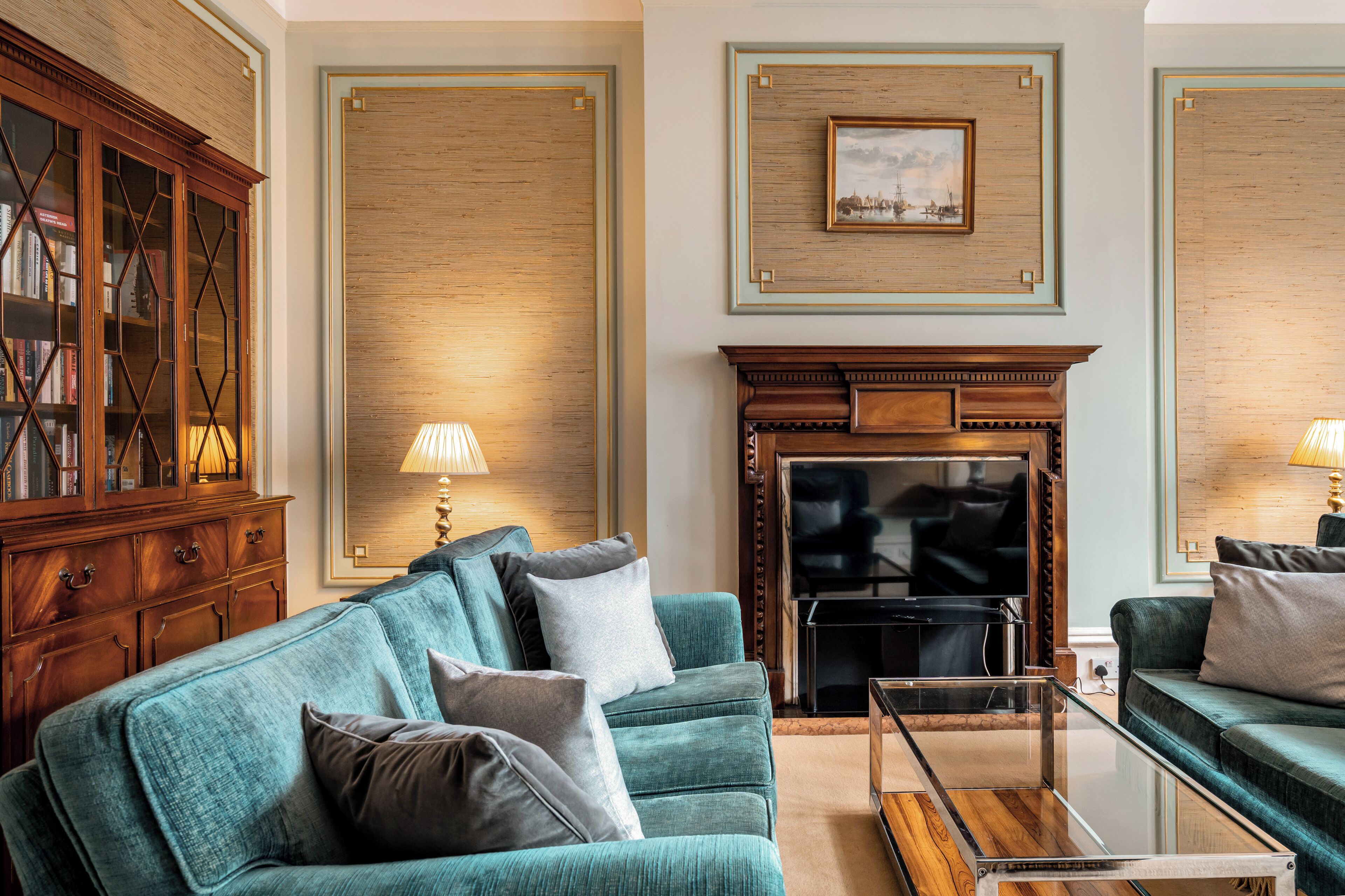 Un salon avec un canapé de couleur turquoise, un meuble en bois, une cheminée et un tableau encadré au mur.