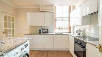 Una cocina compacta con lavadora Bosch, horno integrado y ventana con persianas.