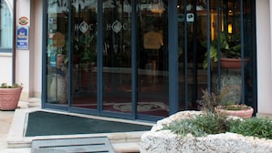 Exterior del Hotel dei Cavalieri con banderas, una amplia entrada de vidrio y plantas en macetas.