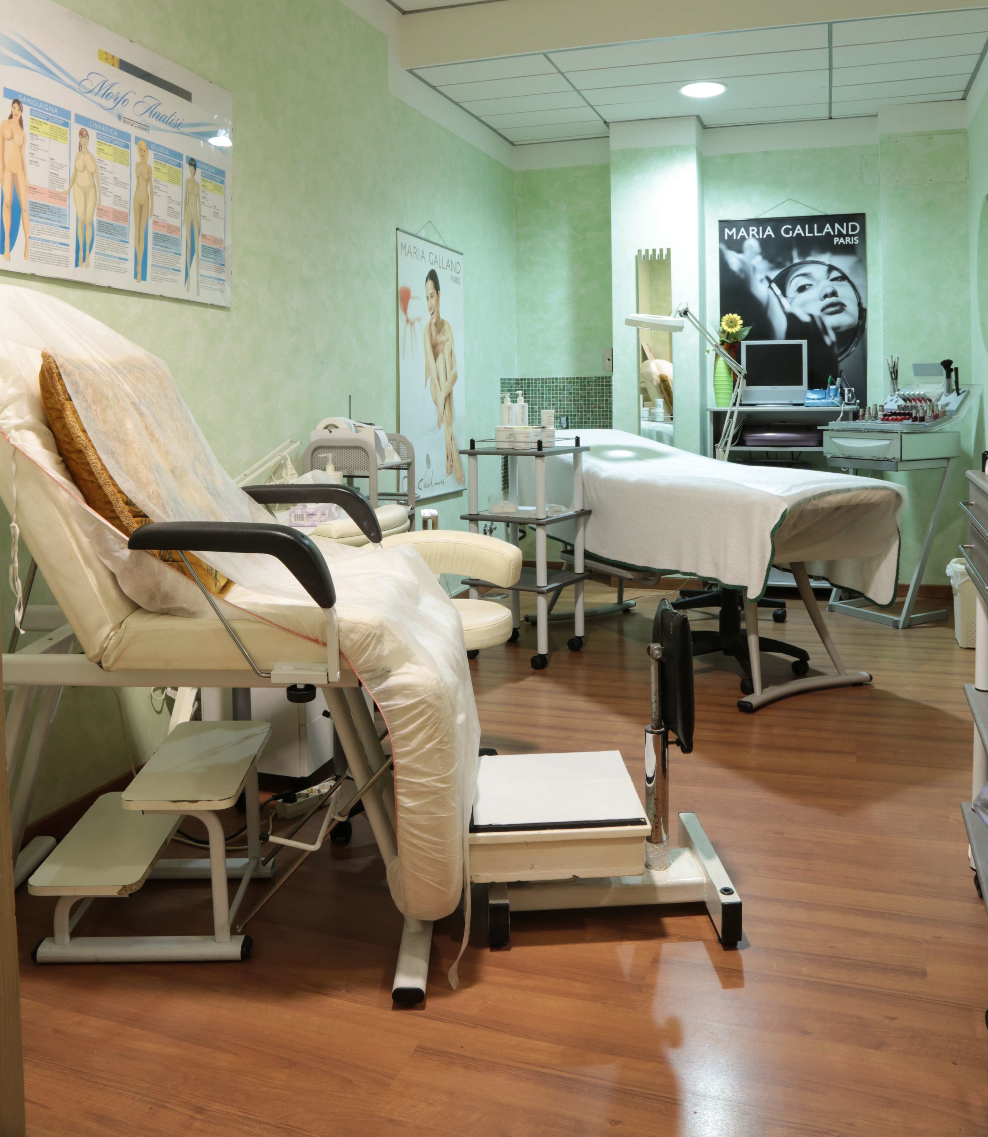 A medical examination room with two examination tables, a computer, and a poster on the wall.