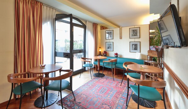 Un restaurant chaleureux avec des tables et des chaises en bois, un tapis à motifs et un canapé de couleur turquoise.