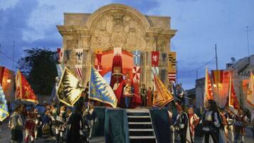 A historical reenactment with participants in period costumes and flags in front of a stone archway.