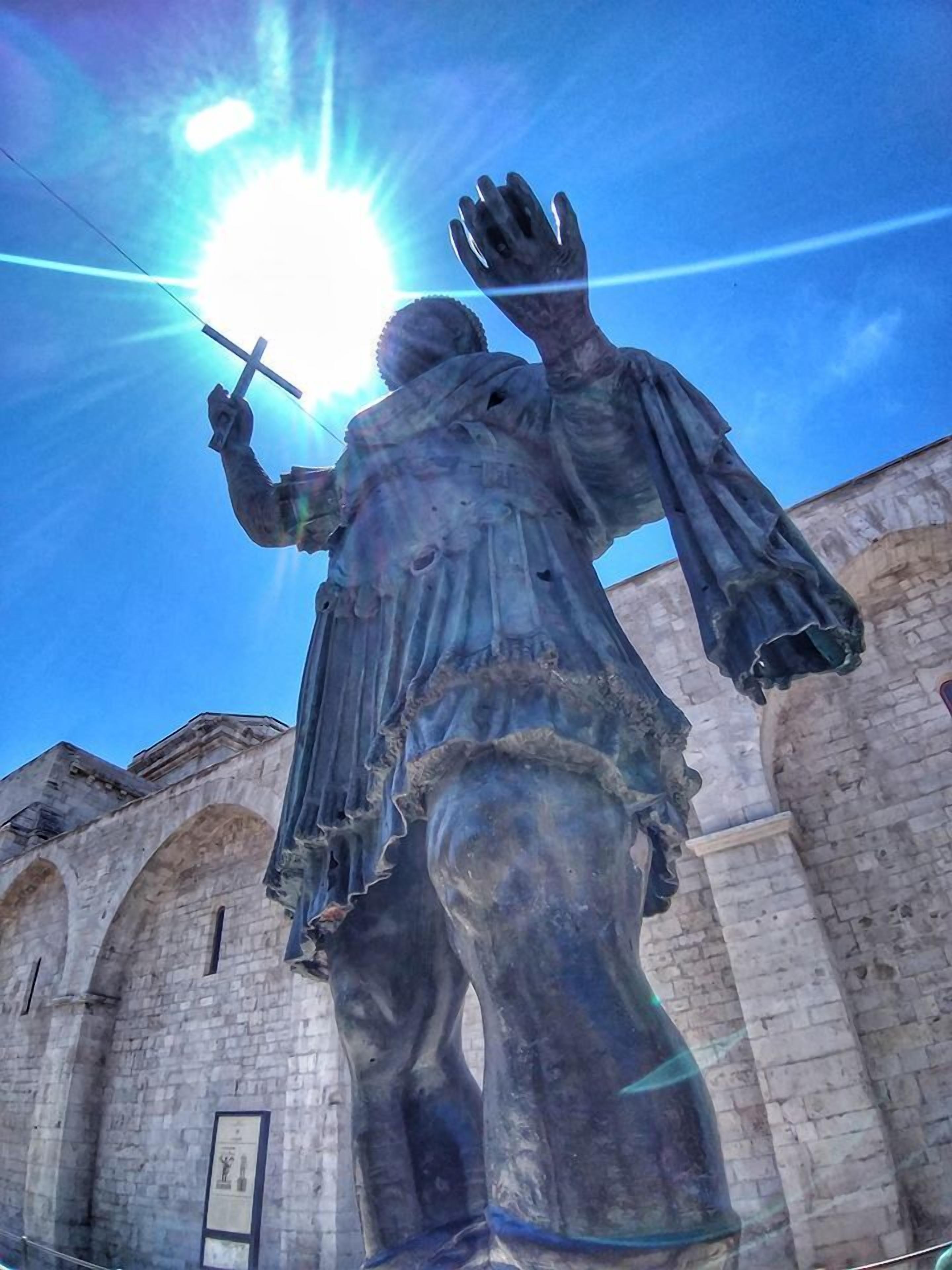 A statue of a figure holding a cross and a book, set against a stone building with arched windows.