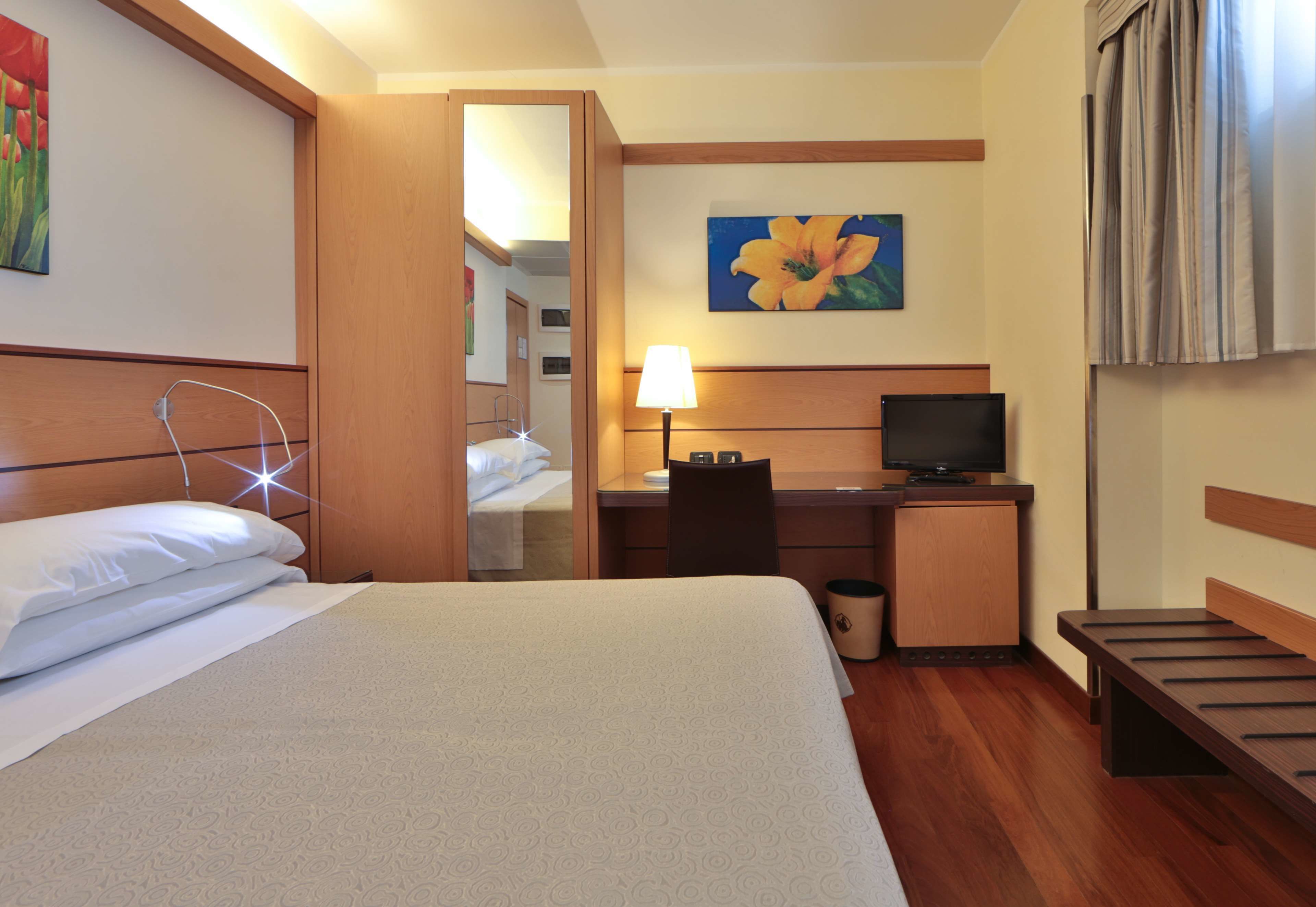 Ein Hotelzimmer mit Bett, Schreibtisch, Stuhl, Lampe, Fernseher und einem Bild an der Wand.