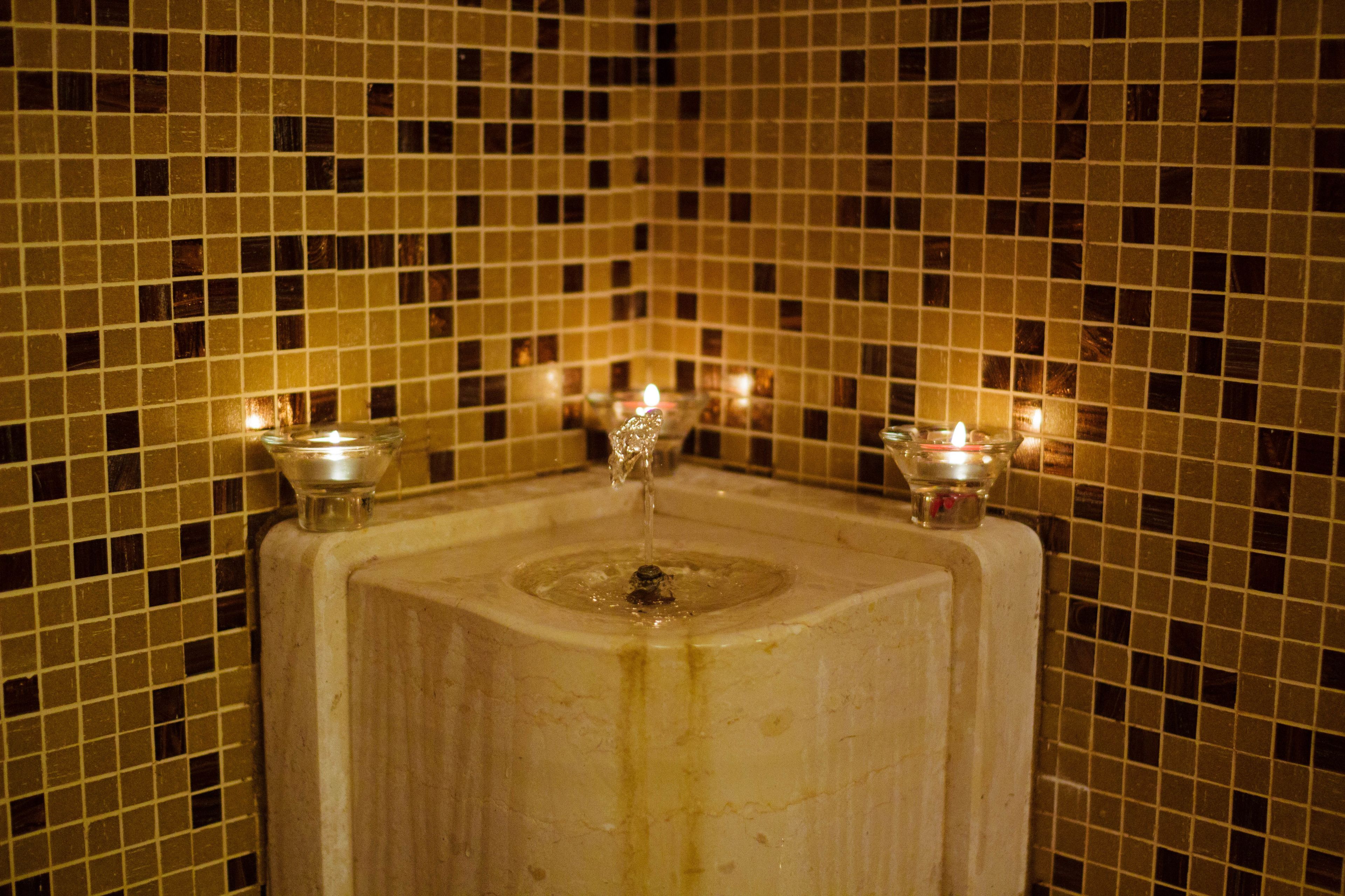 A bathroom with a tiled wall, a sink, and three lit candles.