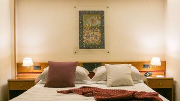 A hotel room with a bed, two bedside tables, a nightstand, a wall-mounted artwork, and a wooden ceiling.