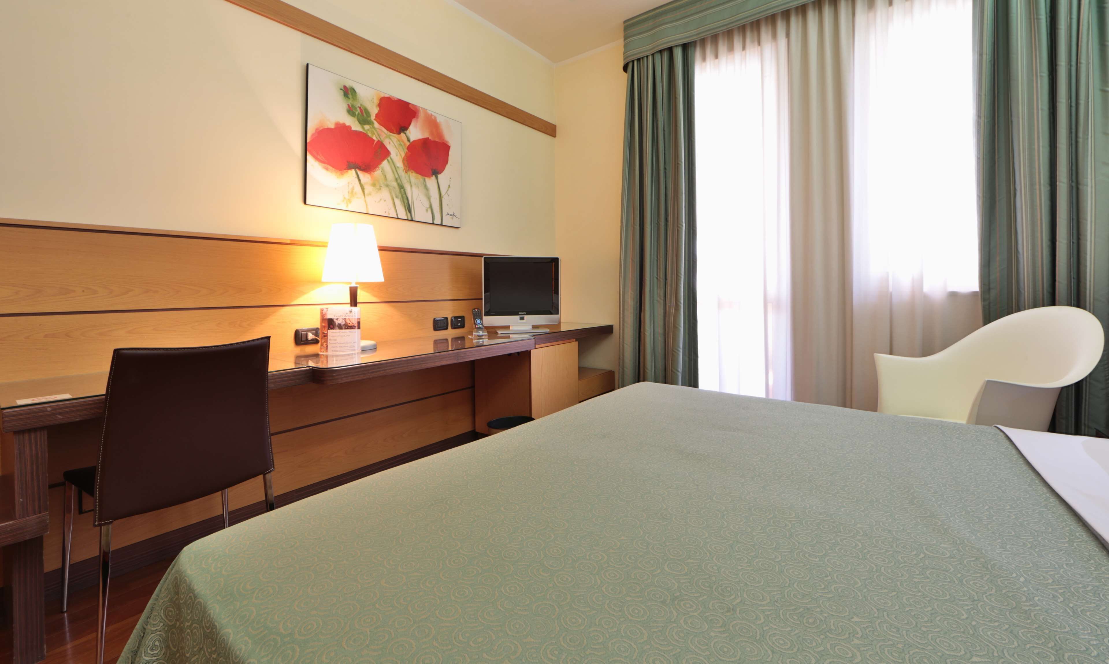Habitación de hotel con cama, escritorio, silla, televisor y un cuadro en la pared.