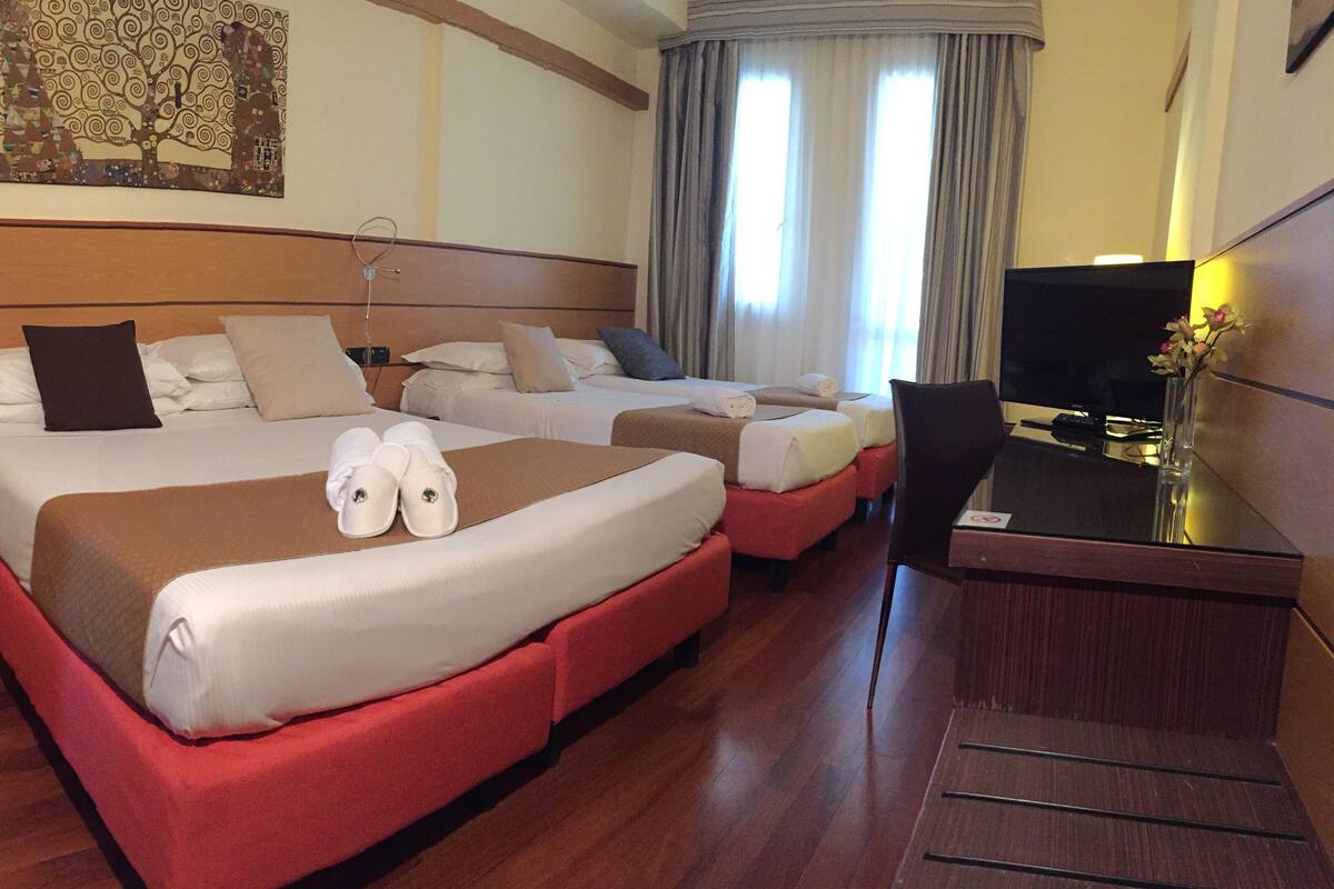Una camera d'albergo con due letti, una scrivania, una TV e un quadro appeso al muro.