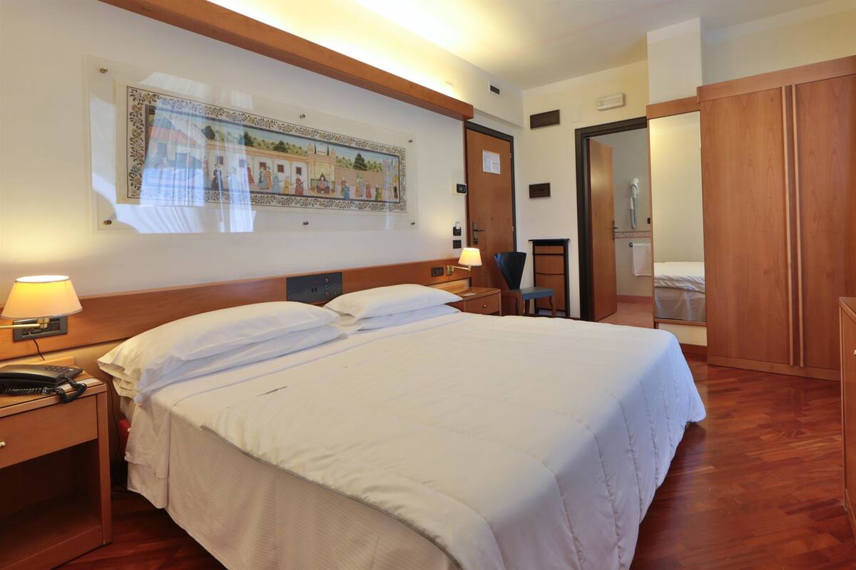 Una camera d'albergo con un letto grande, una scrivania con lampada, una televisione e un armadio in legno.