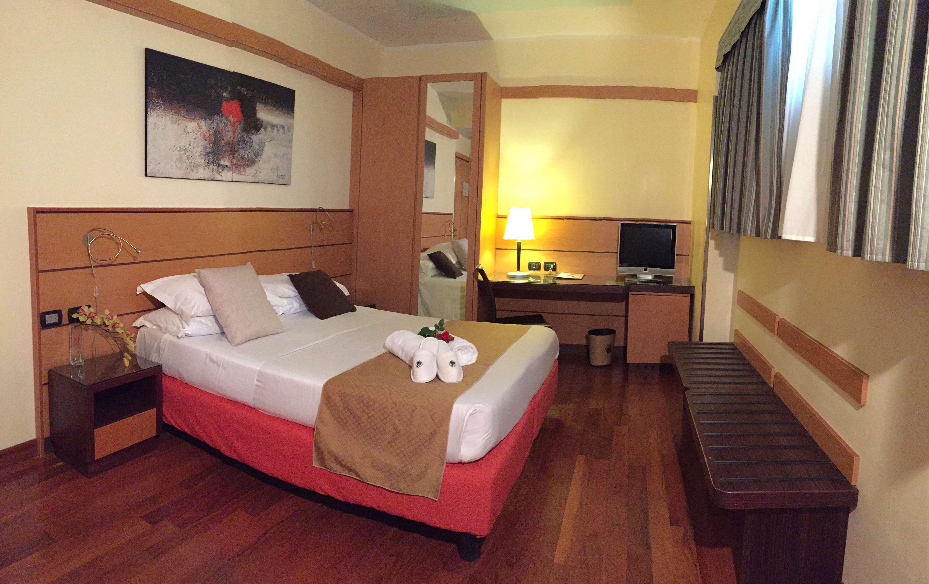 Een hotelkamer met een bed, een bureau, een televisie en een schilderij aan de muur.