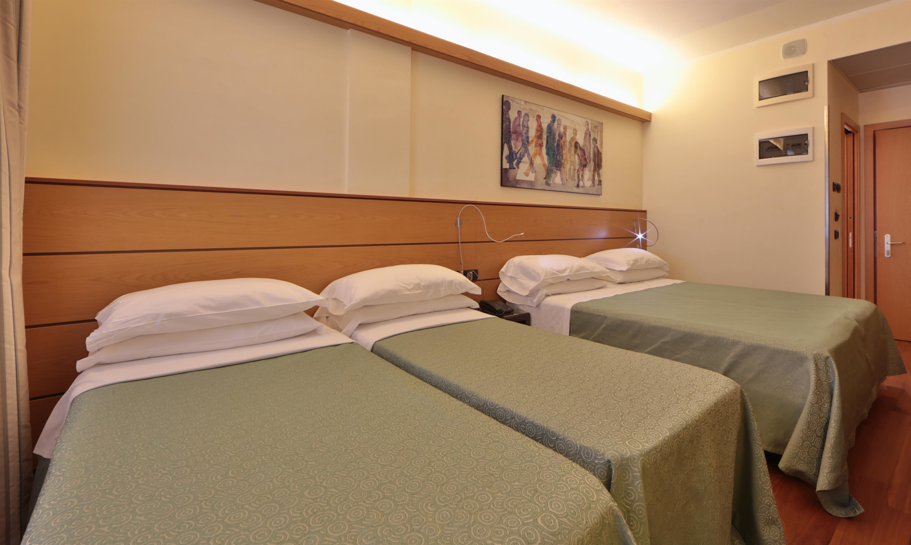 A hotel room with two single beds, a wooden headboard, a painting on the wall, and a door to the right.