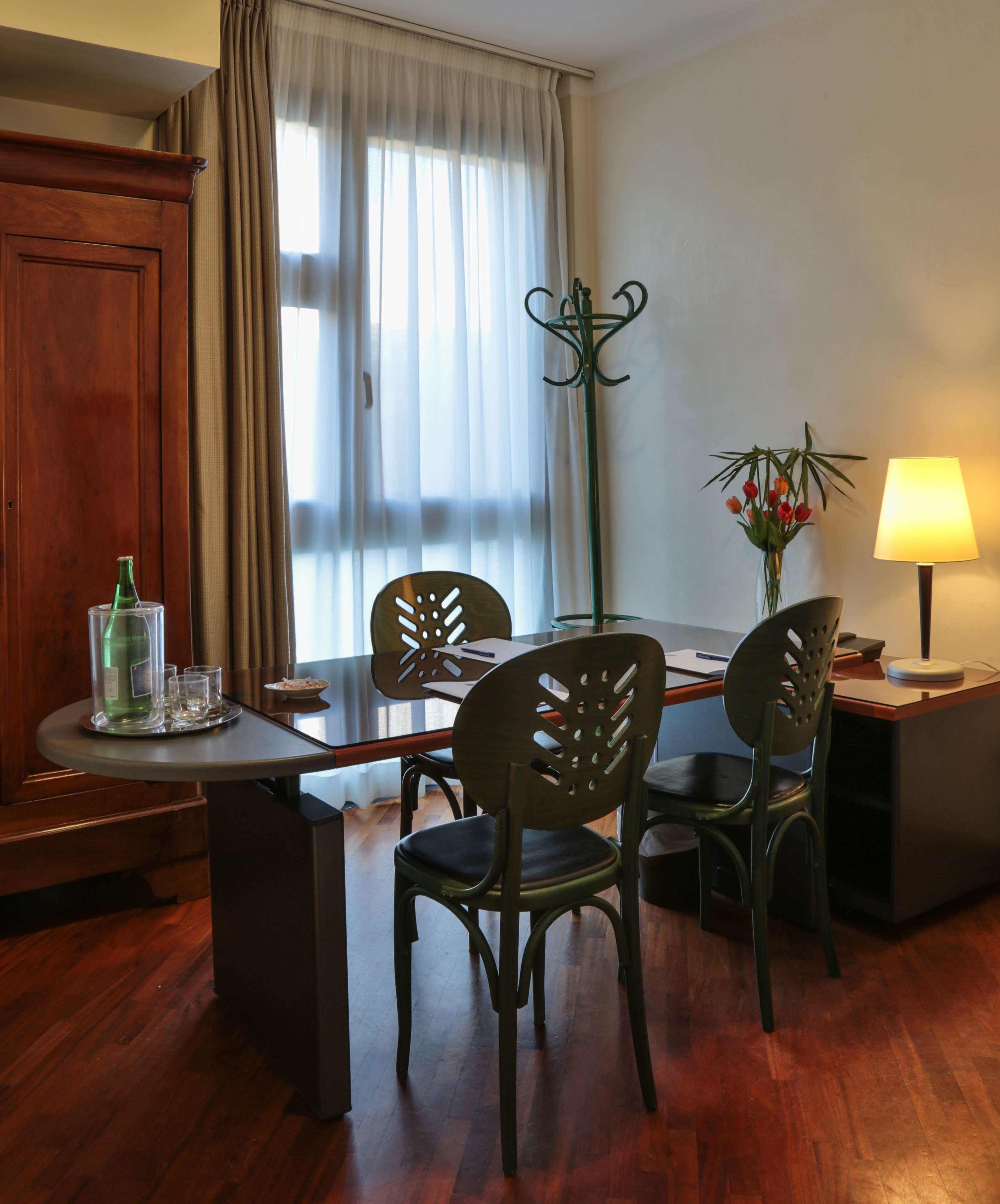 Un comedor con una mesa de madera, cuatro sillas, una lámpara y un florero con flores.