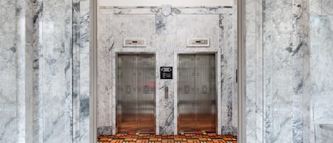 A marble elevator with two doors, a patterned floor, and a plaque on the wall.