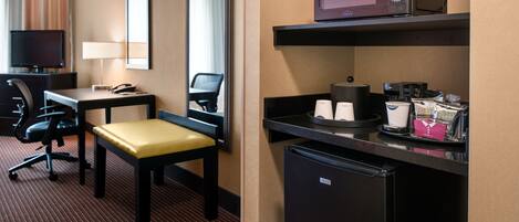 A hotel room with a desk, chair, television, microwave, refrigerator, and a coffee maker.