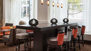 A modern bar area with a long counter, multiple bar stools, and a seating area with orange cushions. - Hampton Inn & Suites Ogden (Ogden)