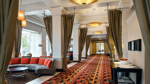 A hotel lobby with a patterned carpet, a sectional sofa, and a long hallway with curtains and pendant lighting. - Hampton Inn & Suites Ogden (Ogden)