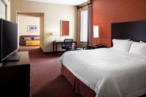 Habitación de hotel con una cama grande, un escritorio con silla, televisor y sofá con cojines.