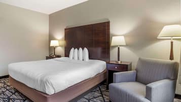A hotel room with a large bed, two bedside tables with lamps, a chair, and a dark headboard.