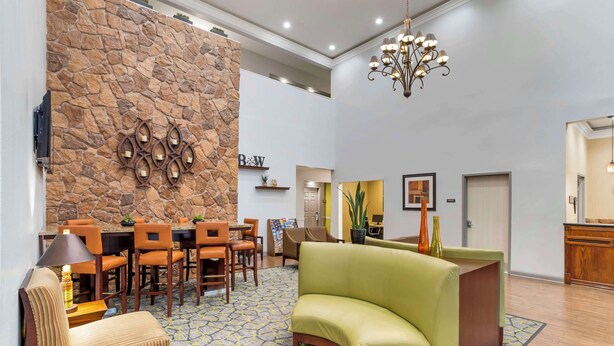 A lobby with a stone wall, a reception desk, a green sofa, and a dining area with wooden chairs and tables. - Best Western Plus Hobby Airport Inn & Suites (Houston)